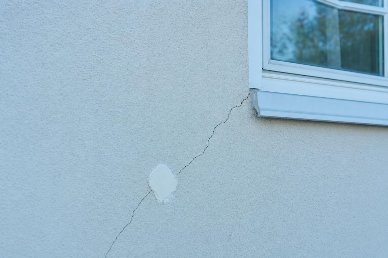 Diagonaler Setzriss im Mauerwerk über einem Fenster, daneben eine Gipsmarke zur Rissbeobachtung (Symbolbild)